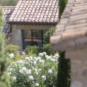 Toiture en tuiles rondes et lauriers blancs devant la façade en pierre. Poutres de récupération