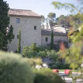 Façade en pierre, cyprès et bains de soleil au bord du bassin. Réhabilitation lourde au pied du village d'Eygalières