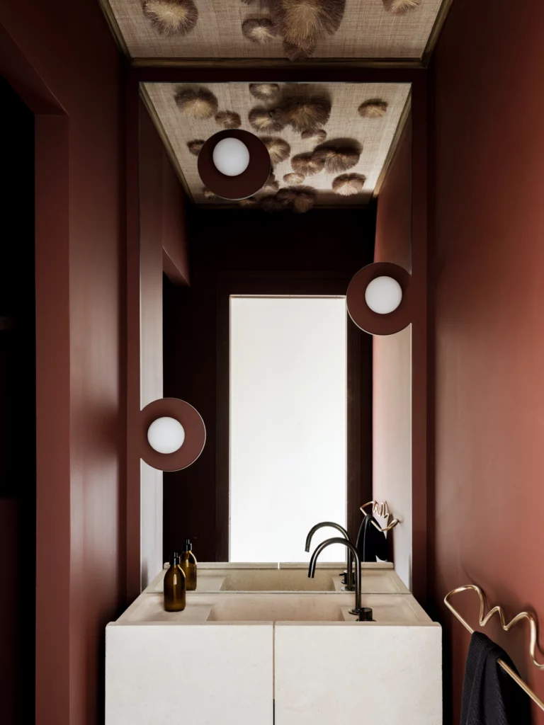 Miroir et lampes rondes. Murs rouge brique : vasque monolithe en pierre, plafond en fibres tressées. Bosc Architectes
