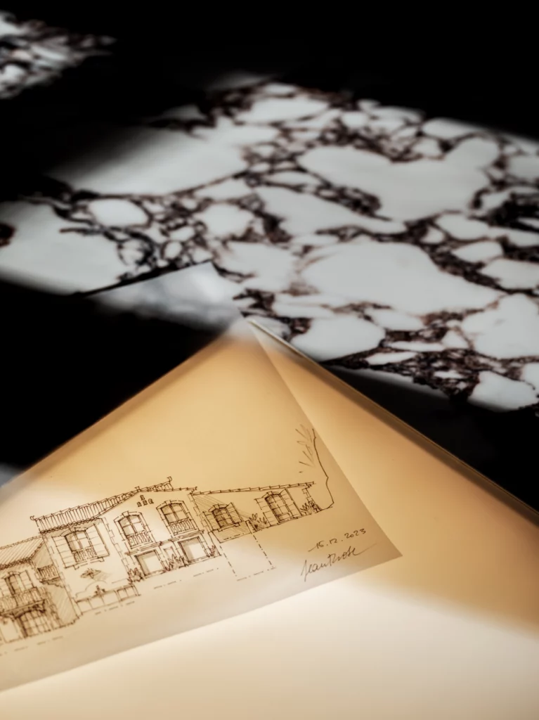 Un dessin d'élévation à la main, daté de décembre 2023, posé sur la table lumineuse dans le marbre. Bosc Architectes